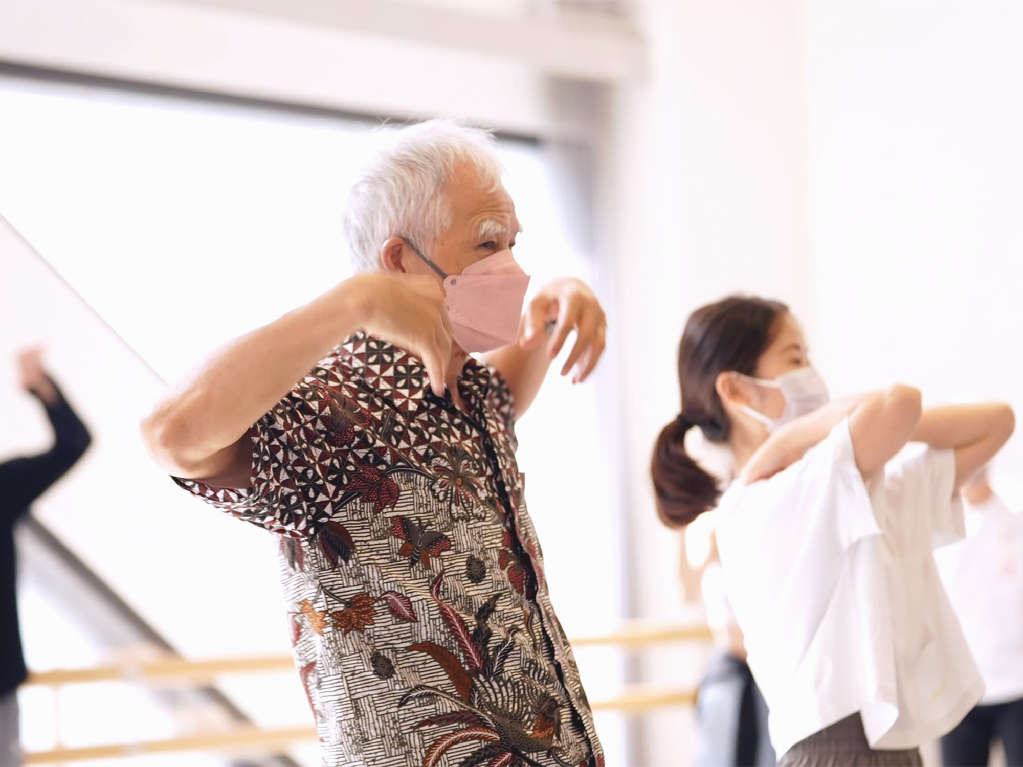 In a dance studio, an old man dancing beside a young lady, side by side, doing similar movements with their hands on their own shoulders, elbows pointing outside, the photo shows that anyone can dance, no matter their respective age, gender and abilities.